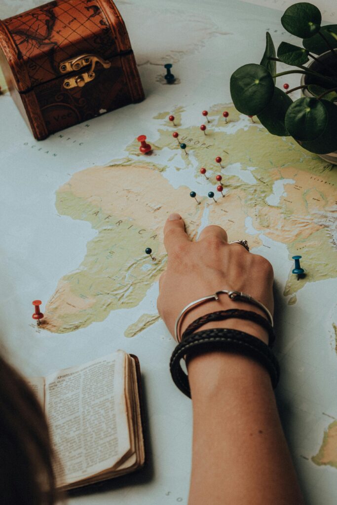 A hand pointing on a world map with colorful push pins, showcasing global destinations.